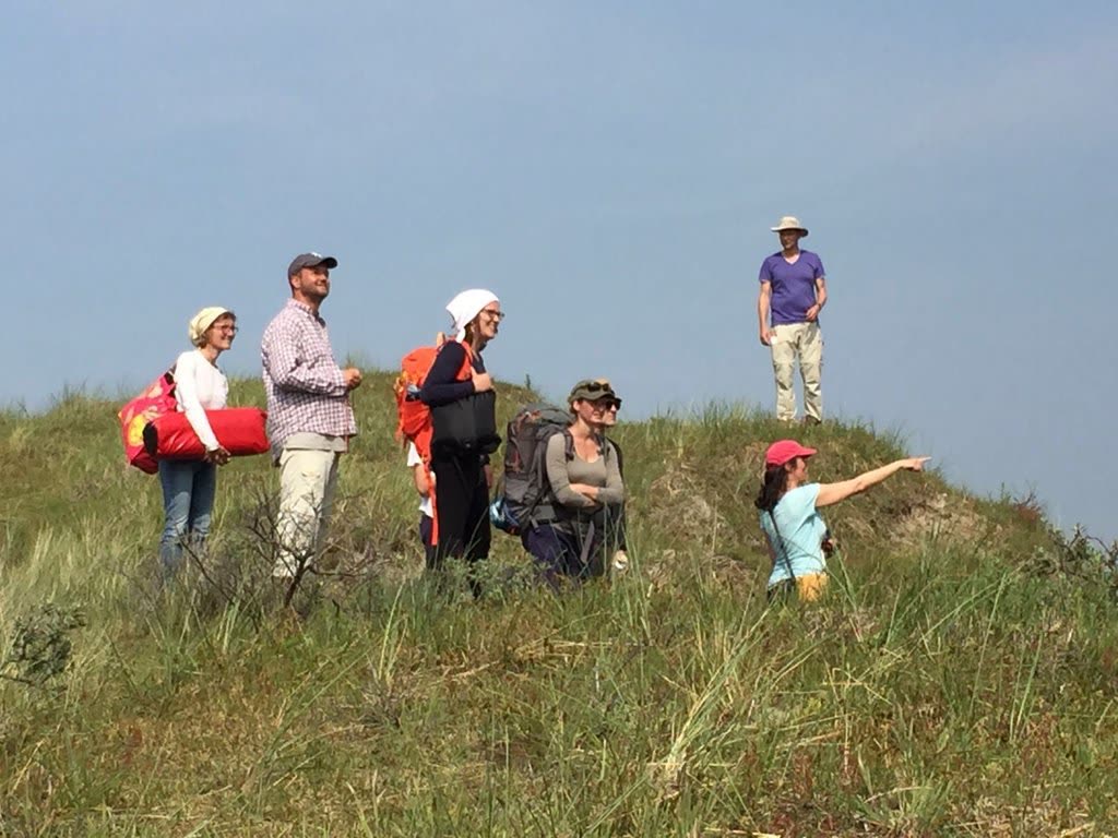 Een kleine groep deelnemers met rugzakken in de duinen; iemand wijst in de verte